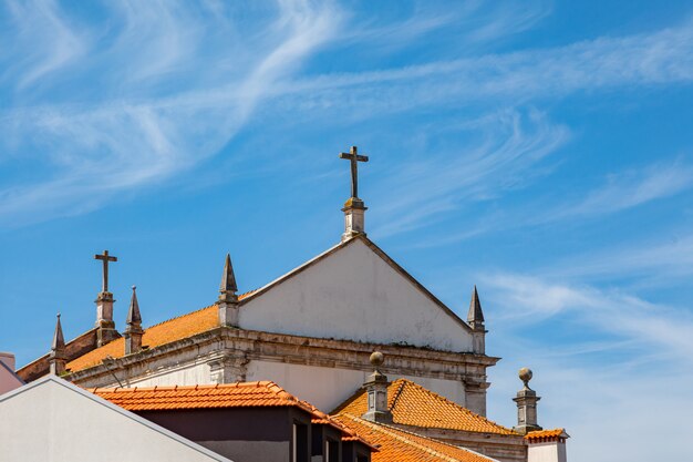 Cruz en el techo de la Iglesia con tejas de color naranja contra el cielo.