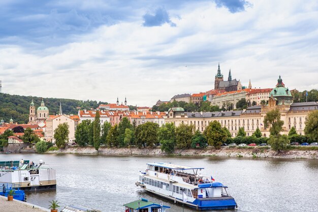 Cruzador de cabine de passageiros em movimento ao longo do rio no fundo da paisagem urbana histórica de Praga, República Checa e céu nublado.