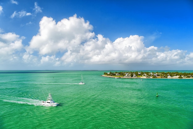 Cruzeiro em barcos turísticos ou iates flutuando pela ilha com casas e árvores verdes em águas turquesa e céu azul nublado, iates e vida nas ilhas ao redor da bela Key West Flórida, EUA