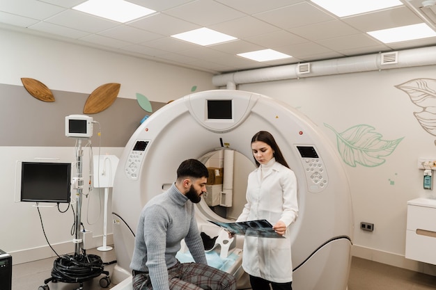 CT Doctor consultando al paciente y mostrando el escaneo de la cabeza de rayos X al paciente en la sala de tomografía computarizada Radiólogo de tomografía computarizada que muestra la radiografía de cerebros al paciente hombre en la sala de escaneo computarizado