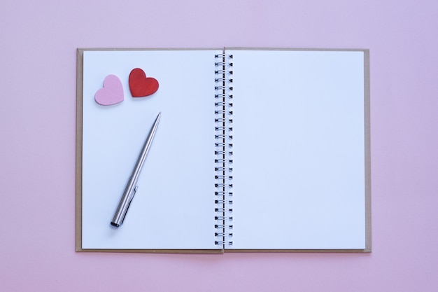 Cuaderno abierto en blanco con corazones rojos y rosados