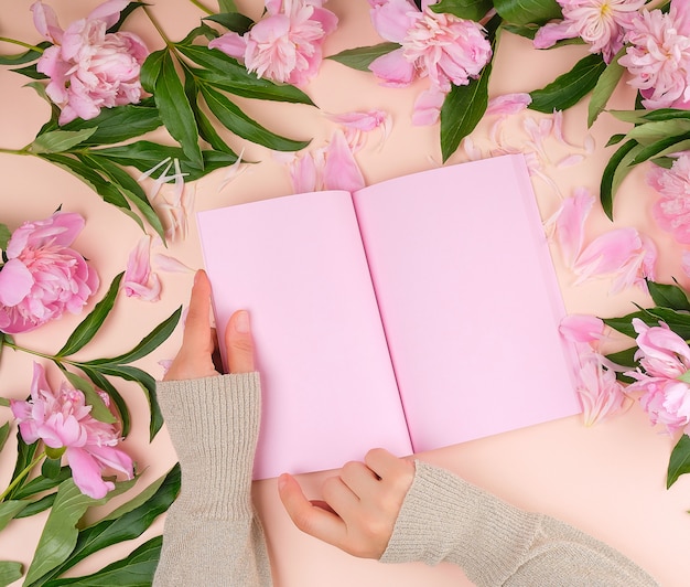 Cuaderno abierto en blanco con hojas rosas y peonías en flor con hojas verdes