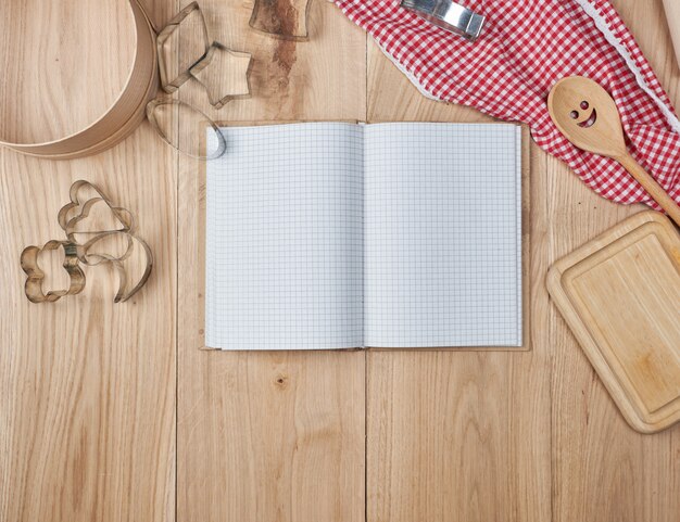 Cuaderno abierto en blanco en línea y accesorios de cocina de madera.