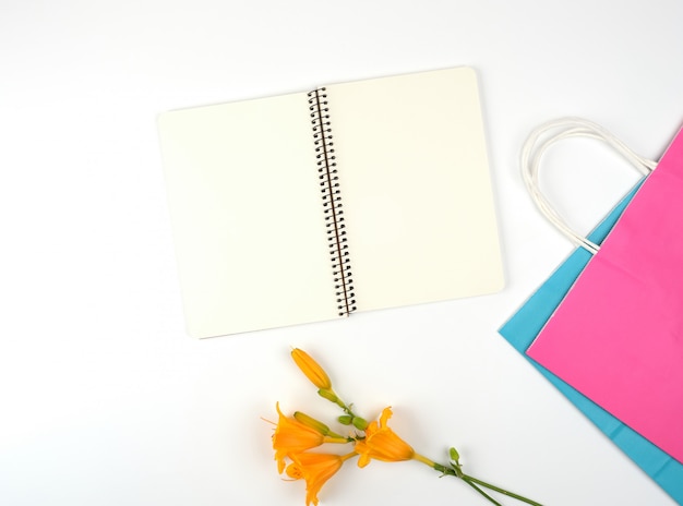 Cuaderno abierto con hojas blancas en blanco y bolsas de papel multicolores