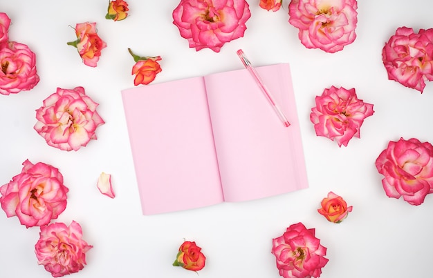 Cuaderno abierto con páginas en blanco rosas y pétalos de rosas rosas