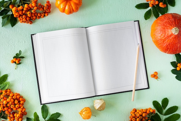 Cuaderno abierto con páginas en blanco sobre un fondo verde con calabazas, manzanas y peras. Maqueta, vista superior. Plano de otoño sentar con ingredientes de la receta.