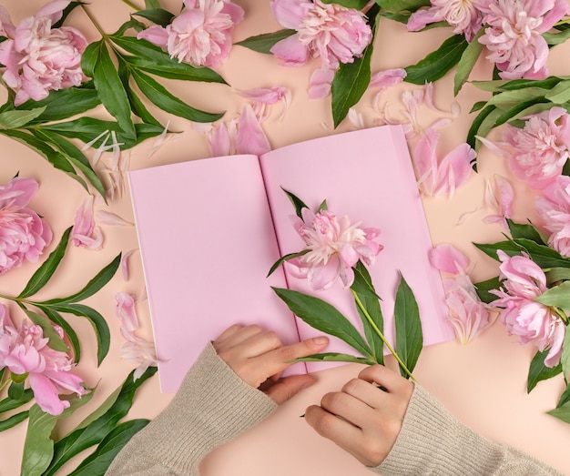 Cuaderno abierto con páginas rosadas vacías y dos manos femeninas.