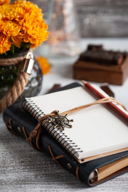 Foto cuaderno abierto vacío y flores de crisantemo naranja sobre mesa rústica.