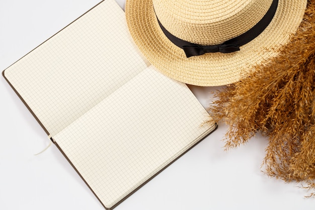 Cuaderno de accesorios para mujer, sombrero, estilo de vida, mujer, descanso, con pasto seco, decoración, endecha plana, estilo de color en el fondo. Viajes, concepto de turismo. Vista superior de accesorios de playa.