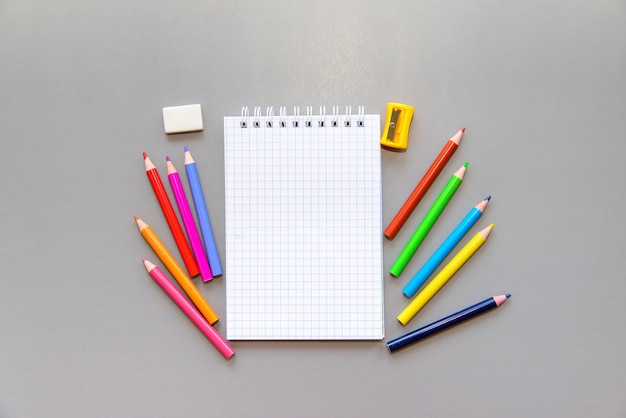 Cuaderno blanco abierto en blanco y útiles escolares sobre un fondo gris. Lápices de colores, borrador, afilado