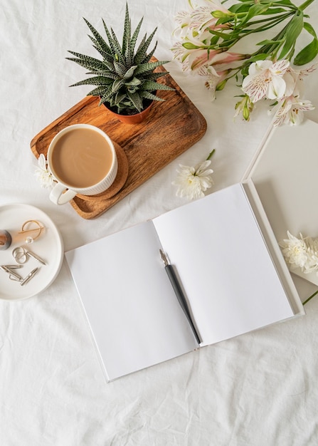 Cuaderno en blanco abierto con café, una planta y flores en una bandeja de madera