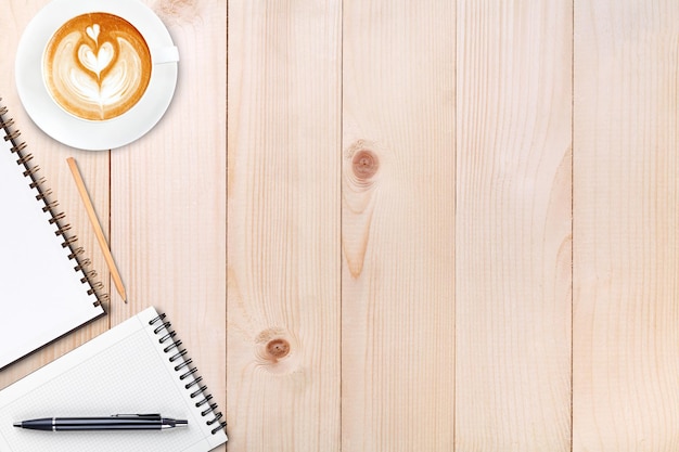 Un cuaderno en blanco abierto con lápiz y una taza de café en la mesa de madera Café con leche en la parte superior