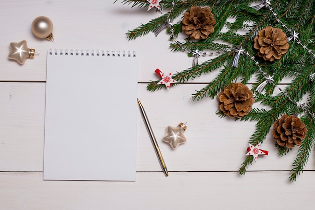 Un cuaderno blanco con un bolígrafo en el fondo de un árbol de Navidad con juguetes conos de pino