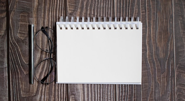 Cuaderno en blanco con bolígrafo, vasos sobre la mesa de madera, concepto de negocio