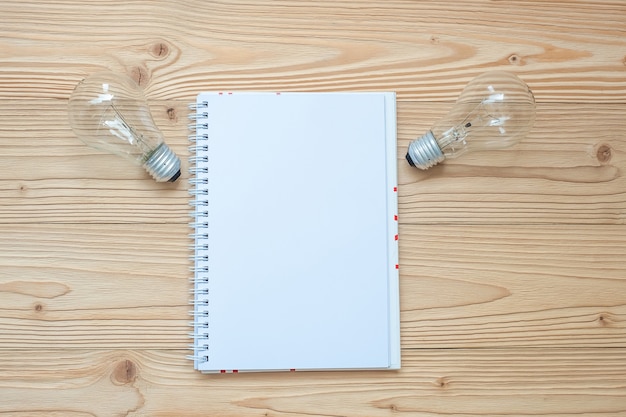 Cuaderno en blanco con bombilla y papel desmenuzado en mesa de madera