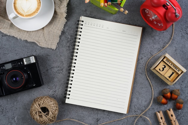 Cuaderno en blanco con cámara vintage, café, reloj rojo y lápiz