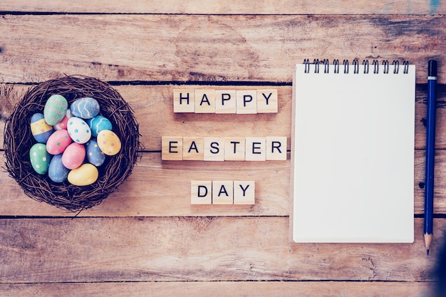 Cuaderno en blanco, colorido huevo de Pascua en el texto de nido y madera para Feliz Día de Pascua sobre fondo de madera con espacio