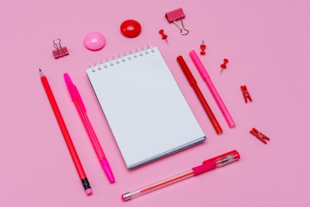 Cuaderno blanco se encuentra en forma de espacio en blanco sobre fondo rosa con bolígrafo rojo con marcadores útiles escolares ...