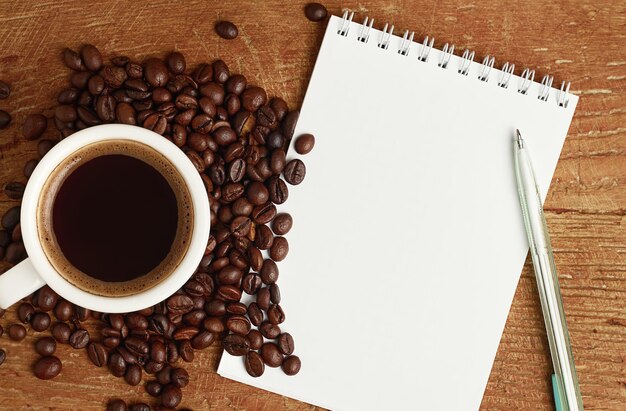 Cuaderno blanco para escribir y café en la mesa de madera.