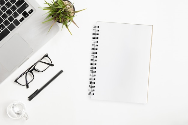 Cuaderno en blanco está encima de la mesa de oficina blanca. Vista superior, aplanada.