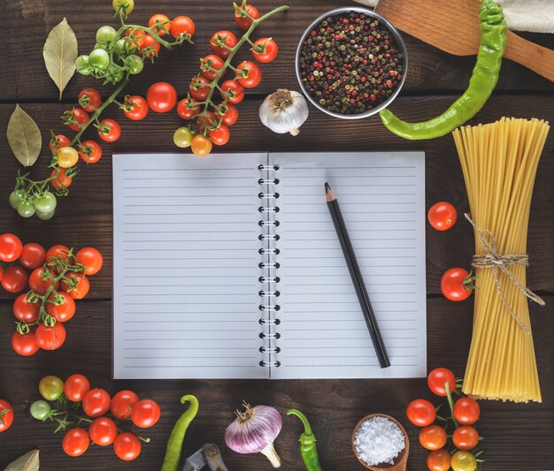 Cuaderno en blanco con hojas blancas, pasta cruda larga e ingredientes para cocinar