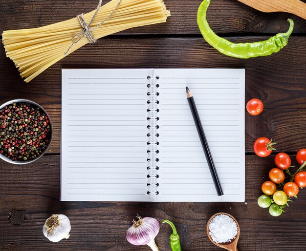 Cuaderno en blanco con hojas blancas, pasta cruda larga e ingredientes para cocinar