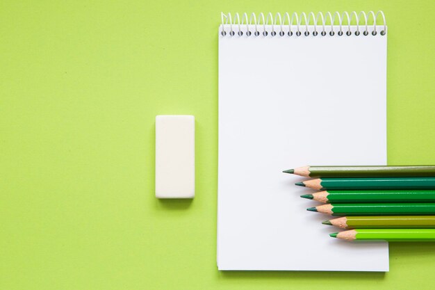 Cuaderno en blanco con lápices de diferentes tonos de verde sobre fondo verde claro