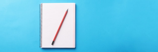 Cuaderno blanco con lápiz de madera se encuentra sobre fondo azul.