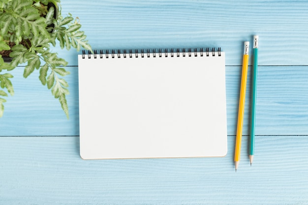 Cuaderno en blanco con y lápiz sobre fondo azul