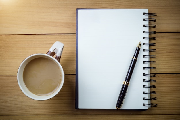 Cuaderno en blanco con las páginas en blanco y con los vidrios al lado de la taza de café en la tabla de madera.