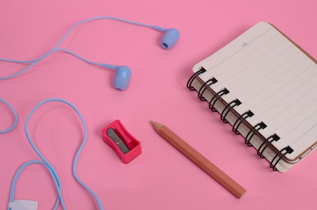 Cuaderno en blanco de papelería y auriculares azules sobre fondo rosa concepto de regreso a la escuela