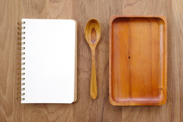 Cuaderno en blanco, placa de madera y cuchara en la mesa