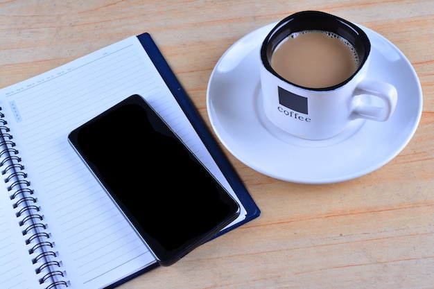 Cuaderno en blanco, pluma estilográfica, smartphone y taza de café en la mesa de trabajo