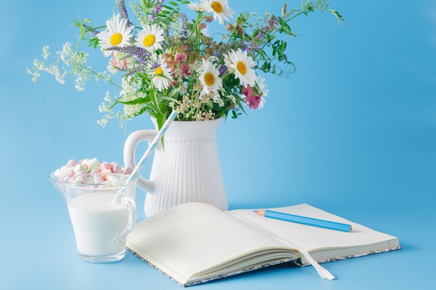 Cuaderno en blanco con pluma y maceta sobre fondo azul.