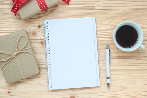 Cuaderno en blanco, taza de café negro y pluma en la mesa de madera