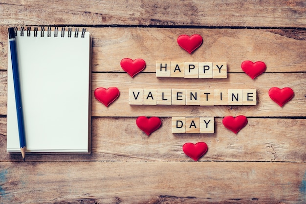 Cuaderno en blanco y texto de madera para Feliz Día de San Valentín con el corazón rojo sobre fondo de madera.