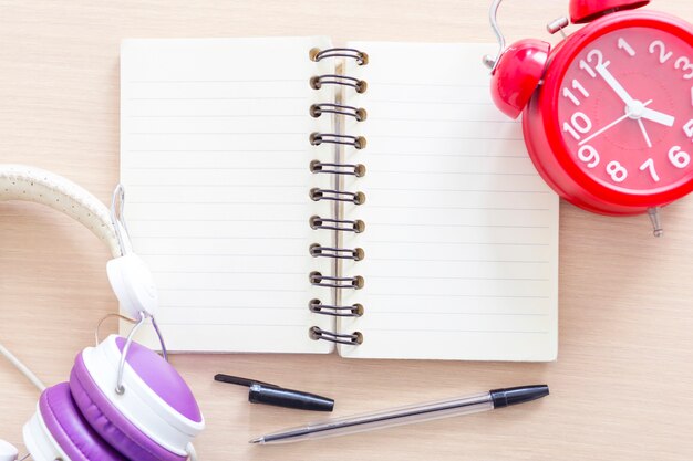 Cuaderno blanco vacío con lápiz, reloj despertador y auriculares.