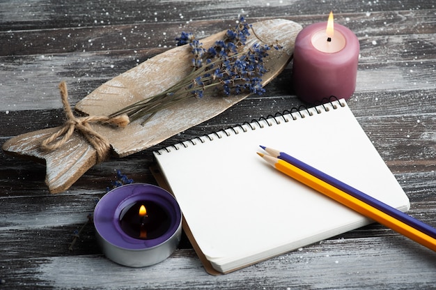 Cuaderno en blanco, velas de aroma púrpura y flores de lavanda secas en la mesa rústica de madera.