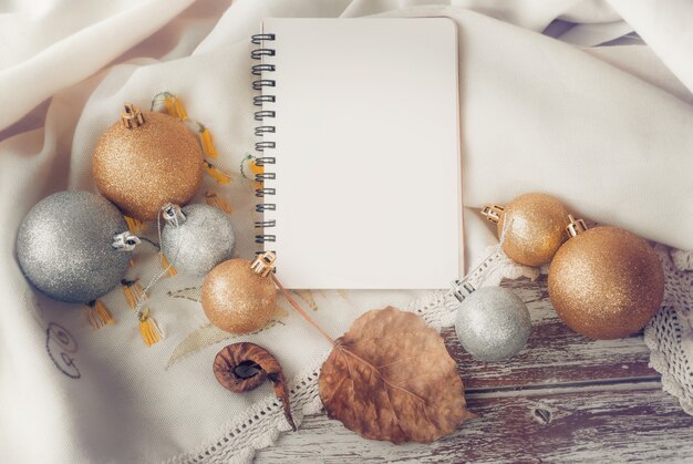 Cuaderno con bola de Navidad de oro y plata en mesa de madera.