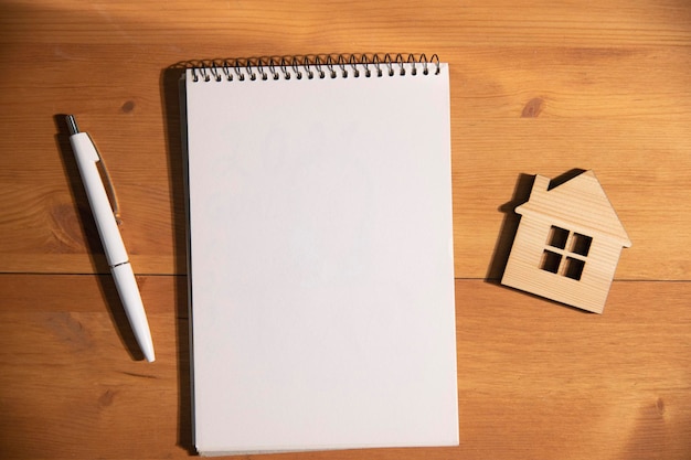 Cuaderno con bolígrafo y casa de madera sobre la mesa.