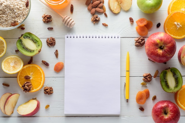 Cuaderno con bolígrafo rodeado de manzanas, kiwi, frutos secos, naranjas y manzanas. El concepto de una dieta saludable y una lista de compras.