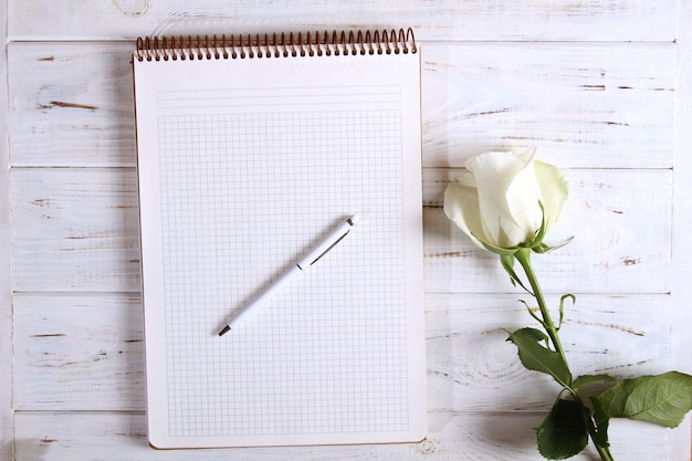 Cuaderno con bolígrafo y rosa.