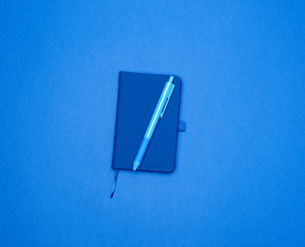 Cuaderno cerrado y bolígrafo azul sobre una superficie coloreada