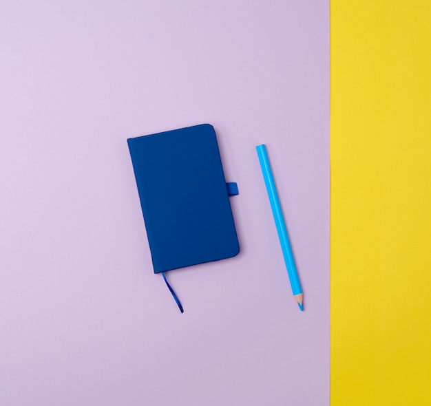 Cuaderno cerrado y lápiz azul de madera sobre una superficie coloreada