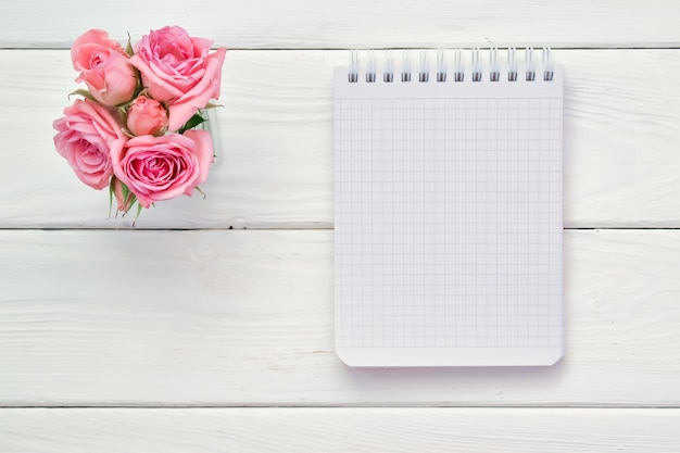 Un cuaderno a cuadros y rosas rosadas sobre una mesa de madera blanca