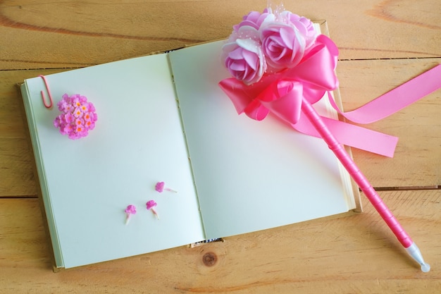 Cuaderno de diario en blanco y flor rosa en mesa de madera