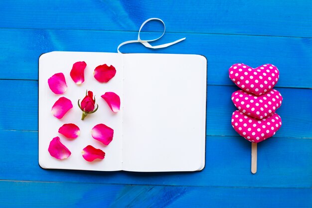 Cuaderno del diario con los corazones de la rosa y de la tarjeta del día de San Valentín en fondo de madera azul.