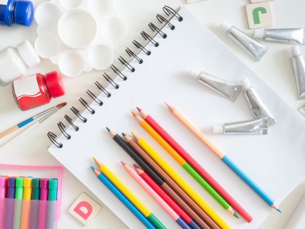 Cuaderno de dibujo, crayones, lápices de colores y papelería escolar en blanco