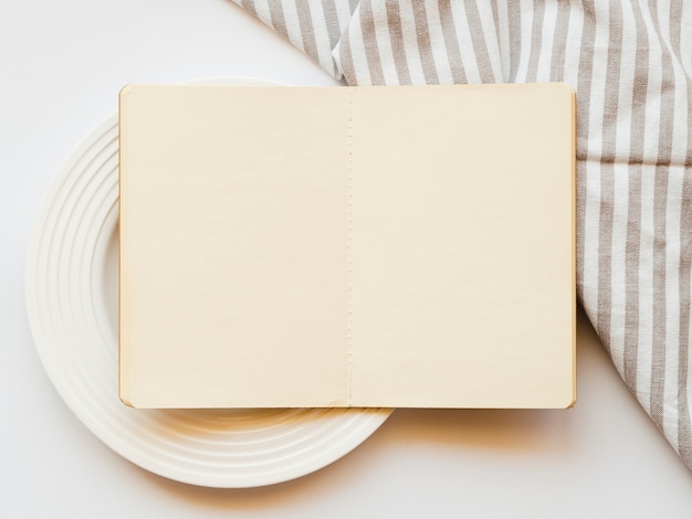 Cuaderno de dibujo marrón pálido en un plato blanco sobre un fondo blanco con un mantel gris y blanco a rayas