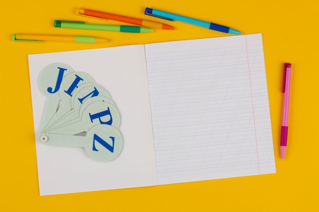 Cuaderno escolar en un fondo amarillo con espacio de copia para texto plumas de colores alfabeto inglés